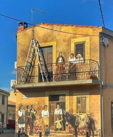 Murales auf Sardinien: Wandgemälde auf ockerfarbener Hauswand mit Dorfbewohnern in traditionellen Trachten und Esel. Murales auf Sardinien: Wandgemälde auf ockerfarbener Hauswand mit Dorfbewohnern in traditionellen Trachten und Esel.