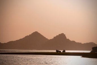 Bergsilhouetten und ein Boot auf einem See im warmen Abendlicht Bergsilhouetten und ein Boot auf einem See im warmen Abendlicht