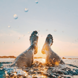Voeten steken vanuit het water omhoog de lucht in met spetter effect op de achtergrond ondergaande zon avondlucht