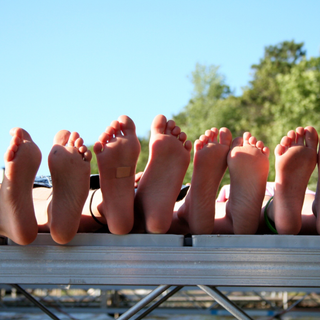 Vier paas blote voeten op een deck achtergrond groene struiken blauwe lucht aan een meer