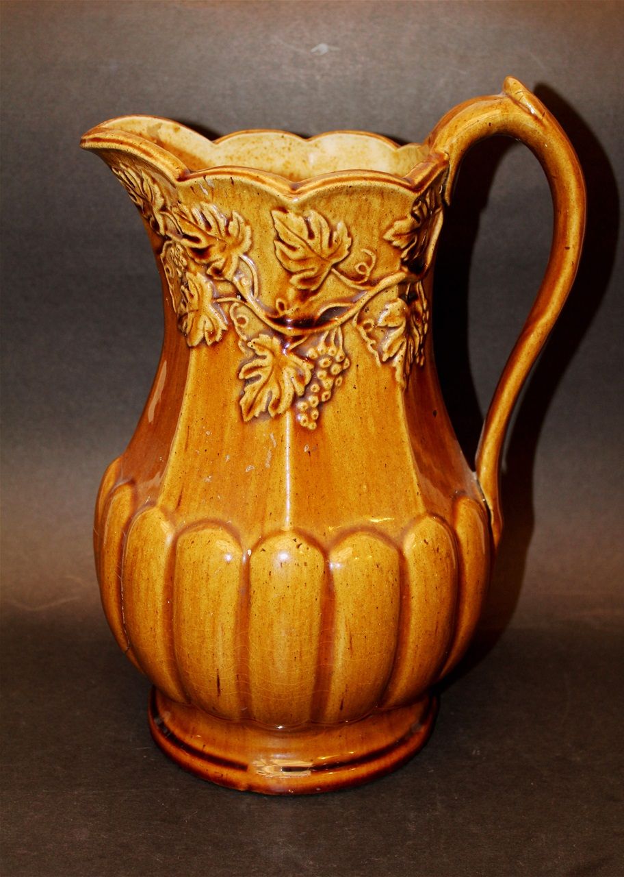 Pichet en terre cuite fine jaune, à glaçure au plomb saupoudrée de manganèse, au motif de bourrelets et feuilles de vigne. Probablement inspiré d'un motif de Charles Coxon de South Amboy, New Jersey. .H. 28 cm.