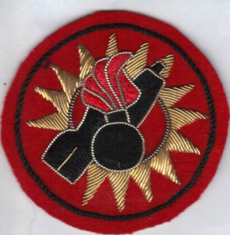 Ammunitionsrydningsofficer
Autoriseret i 1967
Anlagt 1967
AMMUNITIONSRYDNINGSOFFICER 3
Autoriseret:
1967	 
Anlagt:
1967 	
Motiv
Brændende bombe på skråtstillet flyvebombe omgivet af takket krans, alt på cirkulært underlag.
	
Symbolik:
De to bomber refererer til arbejdsopgaverne, og den takket krans refererer til ildglimtet fra en eksplsion.	
Beskrivelse:
På cirkulært højrødt filt i diameter 66 mm, med sort bort en sort brændende bombe med røde flammer, delvist lagt på en skråtstillet højrevendt sort flyverbombe, udført i guldtrækkerarbejde med kontursting om bombe og flyverbomben i snoet tråd, samt den buede inderside har også en tråd af snoet tråd.  

Mærket har aldrig været endeligt godkendt, hvorfor ændringer har været forventet.
Bæring:
Båret af ammunitionsrydningsofficrer, på venstre overærme til uniform M/69 
Varianter:
A/ i guldtrækkerarbejde uden kontursting om de 14 takker, men med indsnit ved bombens hale. Halefinnen udført i et sting med glat tråd.

 
Valgsprog:
Intet
Fremstilling:
Maskinbroderi af fabr. Wermuth, Fredensborg  
