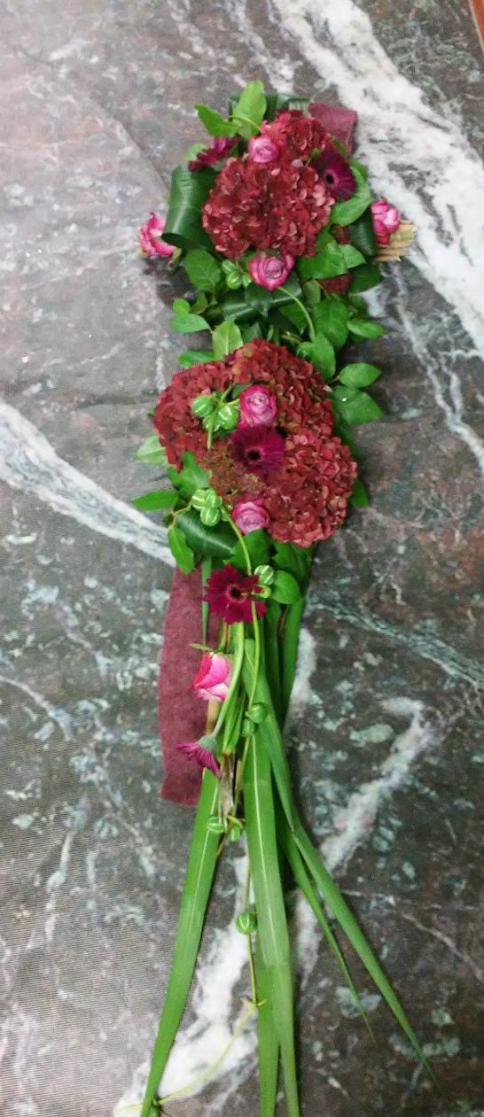 Rouwarrangement gemaakt op rietstengels liggend op vilt. 
Bloemen: hortensia's, rozen, gerbera's, sedum.