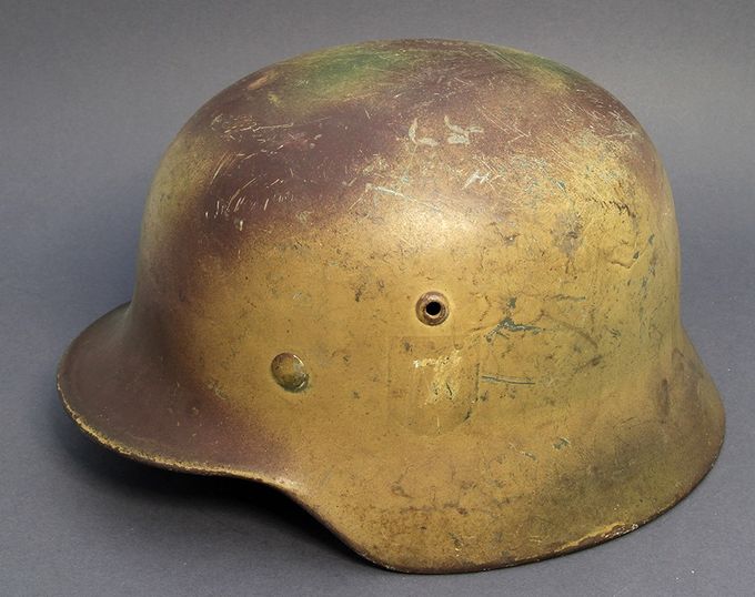 M35 ET64 with a tan base. Brown and green have been sprayed on top. Found with a matching gas mask canister. Notice the ghost decal.