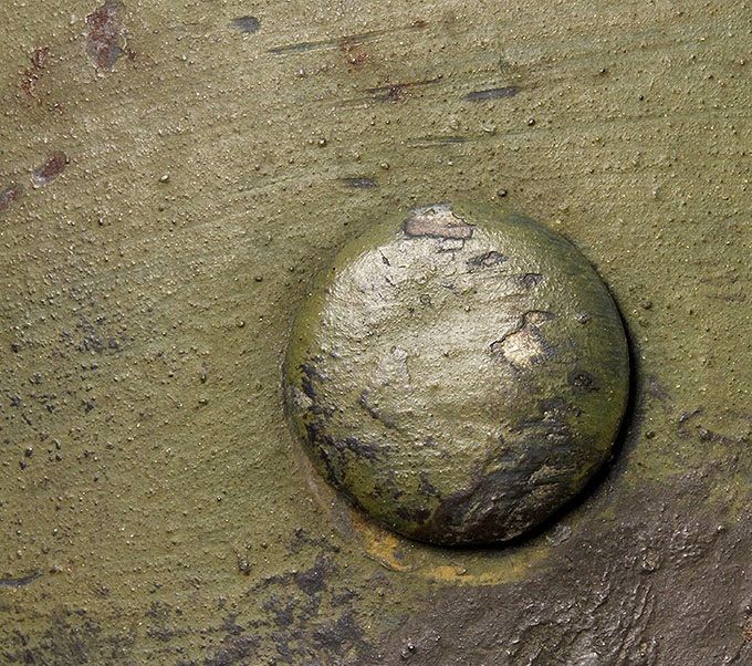Close-up picture of a rivet head and the green and brown paint.