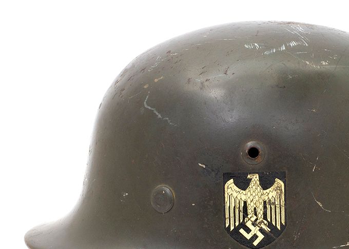 Model 35 (M35) was manufactured from 1935 to 1940 and has a smooth shiny paint which is ranges from bright green to gray-green as shown in the picture above. The generic term for this type of paint is «feldgrau» or field grey. The left side of the M35 helmet features a decal depicting an eagle clutching a swastika. As seen in the photo, the helmet has a vent over the eagle and a rivet placed further down and forward. 