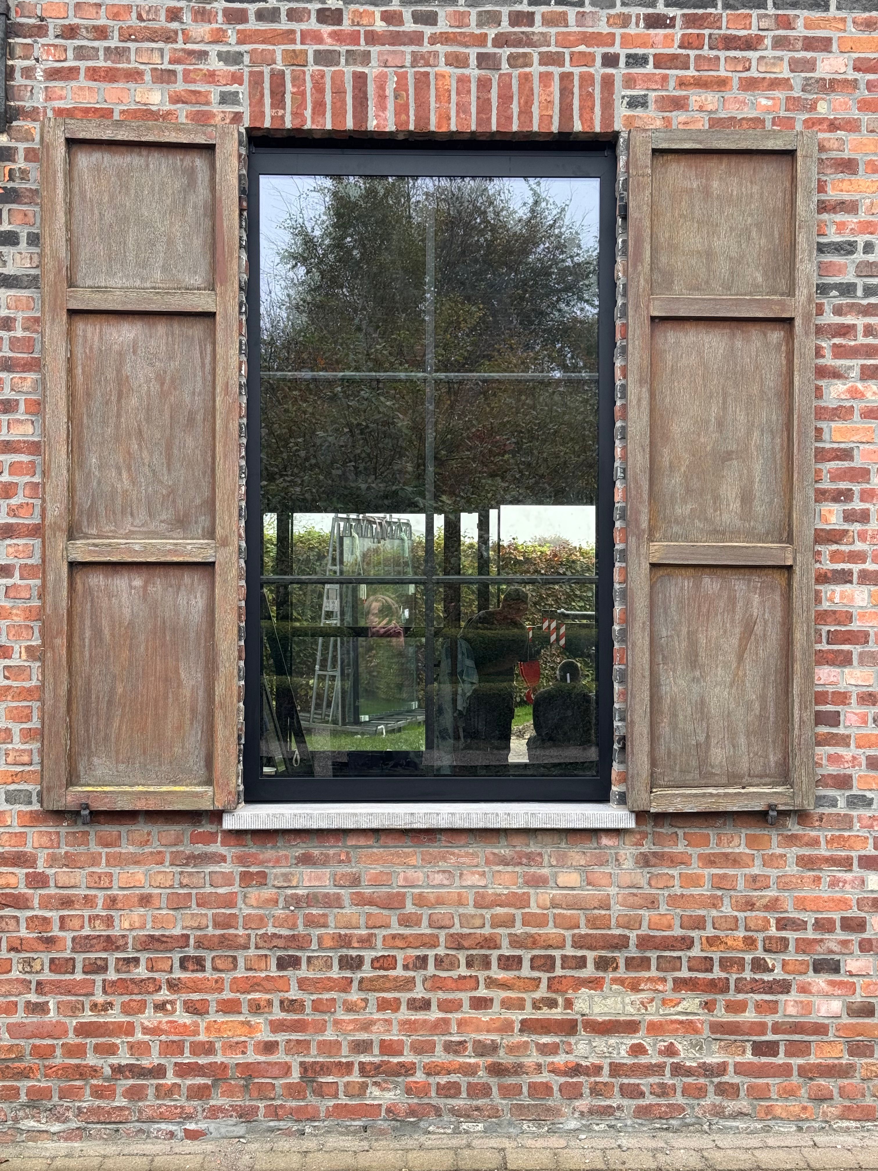 Een strak zwart elegant raam dat in een gerenoveerde hoeve wordt gebruikt met authentieke elemanten zoals houten luiken