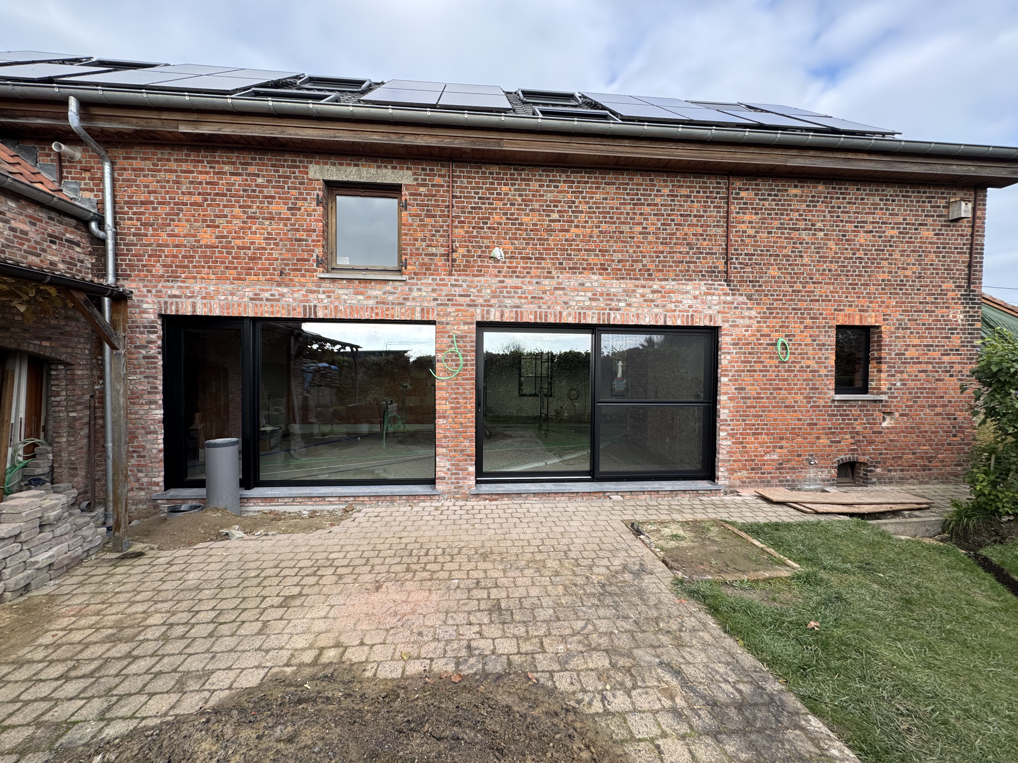 Een strak zwart elegant raam dat in een gerenoveerde hoeve wordt gebruikt met authentieke elemanten zoals houten luiken