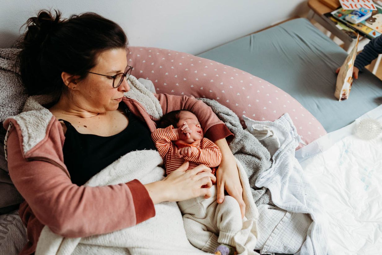 Mutter kuschelt mit Baby im Bett - dokumentarische Wochenbettfotos Muc