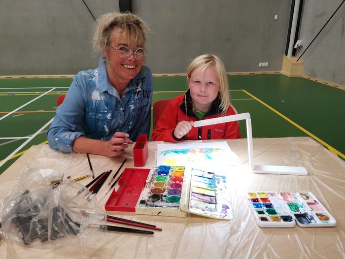 Susanne Brosbøl med børnekunst, mens forældrene kigger på udstillingens mange 