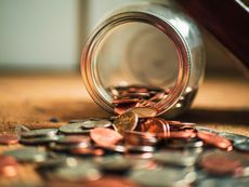 A glass jar with a meal rim on its side with coins spilling out