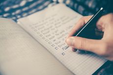 A hand holding a pen and writing in an out-of-focus notebook