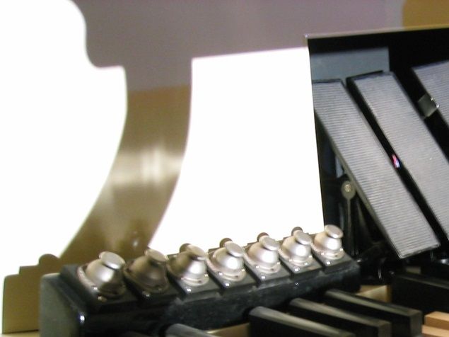 The crescendo shoe (photo, red arrow) is a device found in pipe organs of medium to large size which is operated by the organist's right foot in the same manner as a swell shoe; it selectively adds stops and couplers when the shoe is depressed toward the horizontal and retires them when it is drawn backward to a more vertical position; many larger electronic organs are also fitted with this device.
The crescendo shoe is situated to the far right of any other swell shoes and typically has a slightly raised surface to make it easier for the organist to find it with the right foot without looking down; it is also typically supplied with a display to indicate to the organist how far open or closed it is at any given moment.
As Ed Sullivan would say, this device is, in a very real sense, 