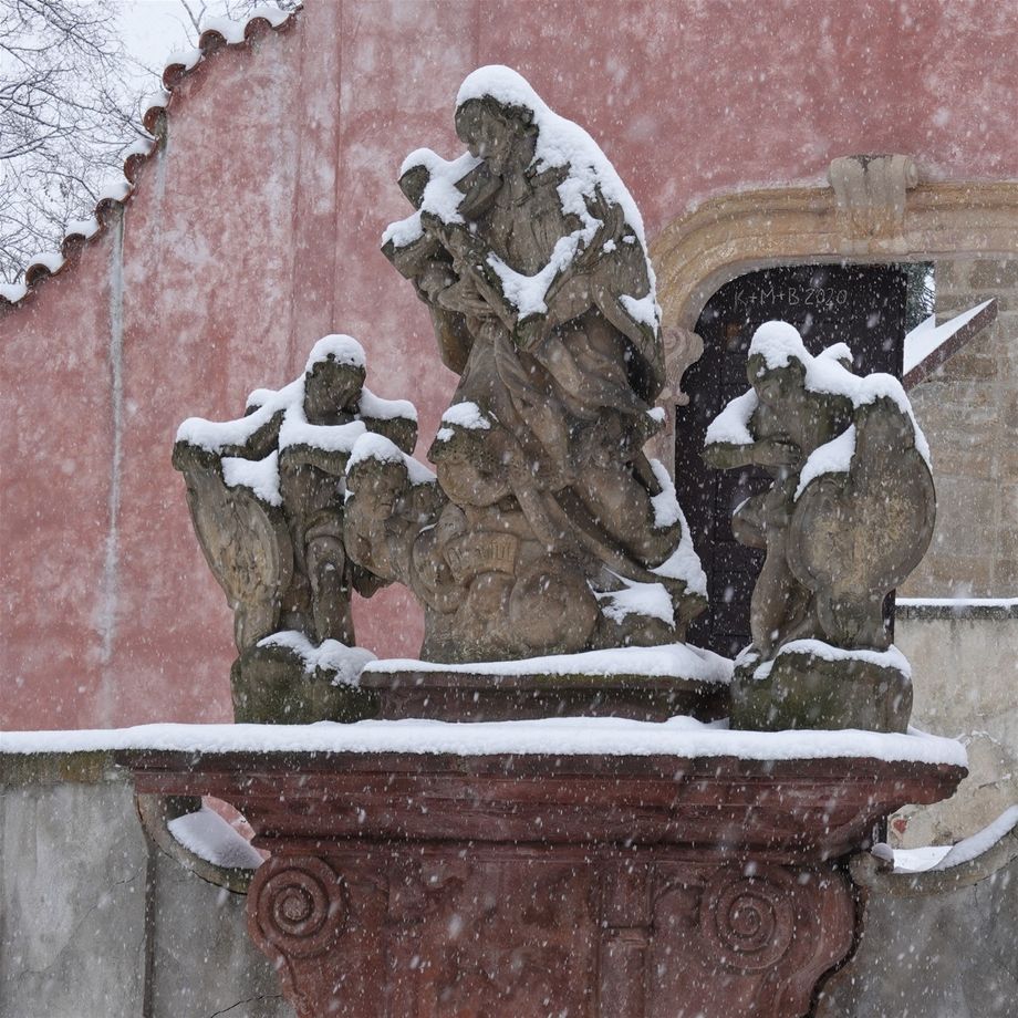 4.12.2021 Tismice, bazilika Nanebevzetí Panny Marie. Velké sněhové vločky zasypávají krajinu a během několika hodin vytvoří dojem vánoční idylky. Autobus z Brodu doklouzal přes závěje do Tismice, silničáři zase zaspali. Z kostela, který budí dojem uzavřené pevnosti, odolávající hektickým vlnám dnešní doby, zní zpěv. Kopie sochy tismické Madony shlíží s klidem, laskavostí a jistotou originálu na předvánoční ruch ve svém zorném poli. Zítra bude druhá adventní neděle, i když sněhová nádhera do večera roztaje. GPS 50.0558286N, 14.8218403E