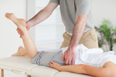 A chiropractor stretches a female customer's leg in his surgery