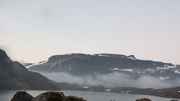 Toppen av Keipen midt i bildet en sommernatt. Bildet tatt med Hjelmevatnet i forgrunnen. Selve veien mot Keipen vil gå helt mot venstre i bildekanten inn dalen der tåka ligger
